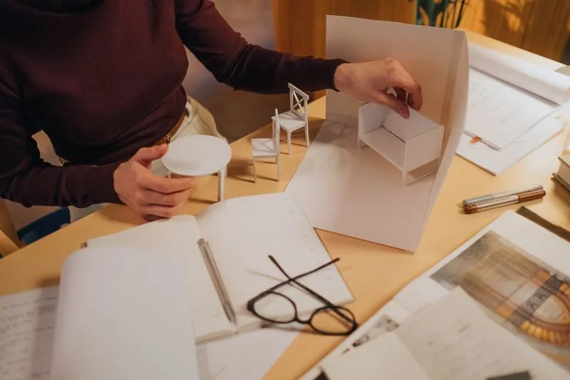 Two people working over drawings and a small model at a desk